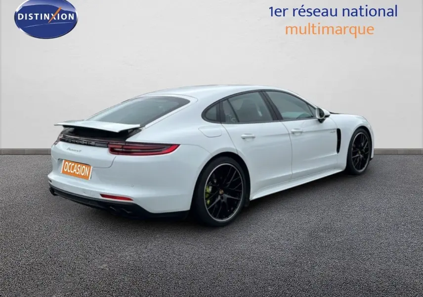Vue 3/4 arrière droite d'une Porsche Panamera 4 E-Hybrid blanche avec jantes noires sport et aileron relevé.