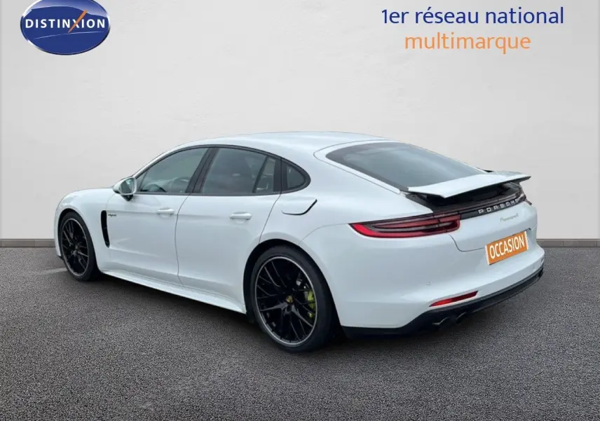 Vue 3/4 arrière droite d'une Porsche Panamera 4 E-Hybrid blanche avec jantes sport noires et aileron déployé.