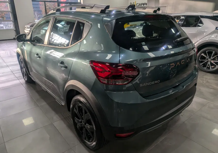 Vue 3/4 arrière gauche d'une Dacia Sandero Stepway TCe 110 vert cèdre avec jantes noires et toit ouvrant en showroom.