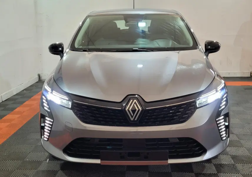 Renault Clio gris foncé vue de face avec phares LED allumés dans un garage intérieur.