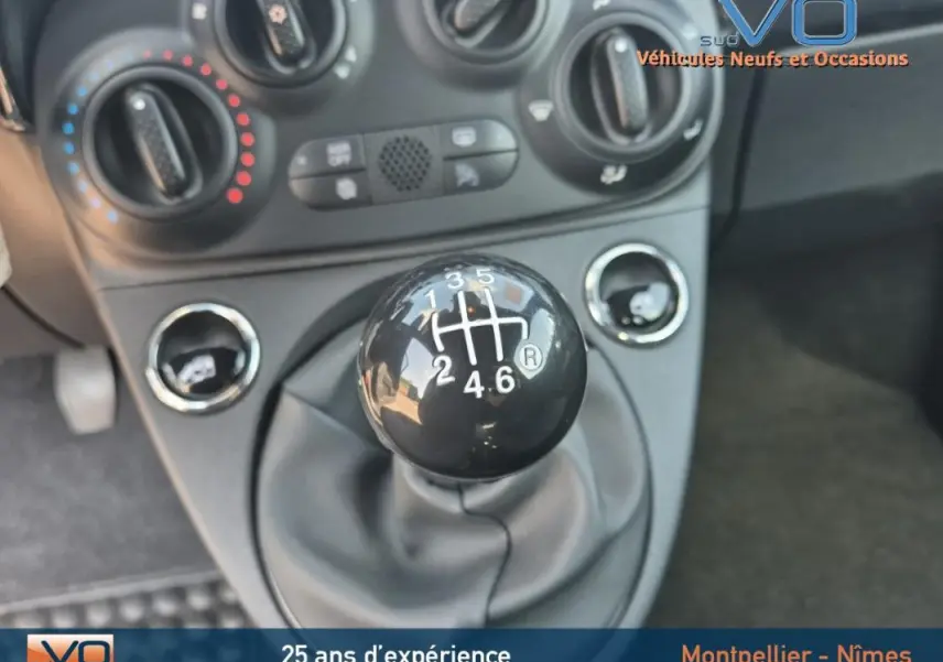 Gros plan sur le levier de vitesses manuel noir de la FIAT 500C 2024, avec commandes de climatisation en arrière-plan.
