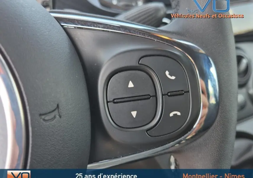 Gros plan sur les commandes de téléphone et volume au volant d'une FIAT 500C noire 2024 hybride essence.