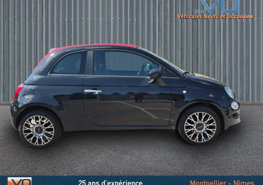 Profil côté gauche de la FIAT 500C noire 2024 avec toit rouge et jantes distinctives, sur fond industriel.