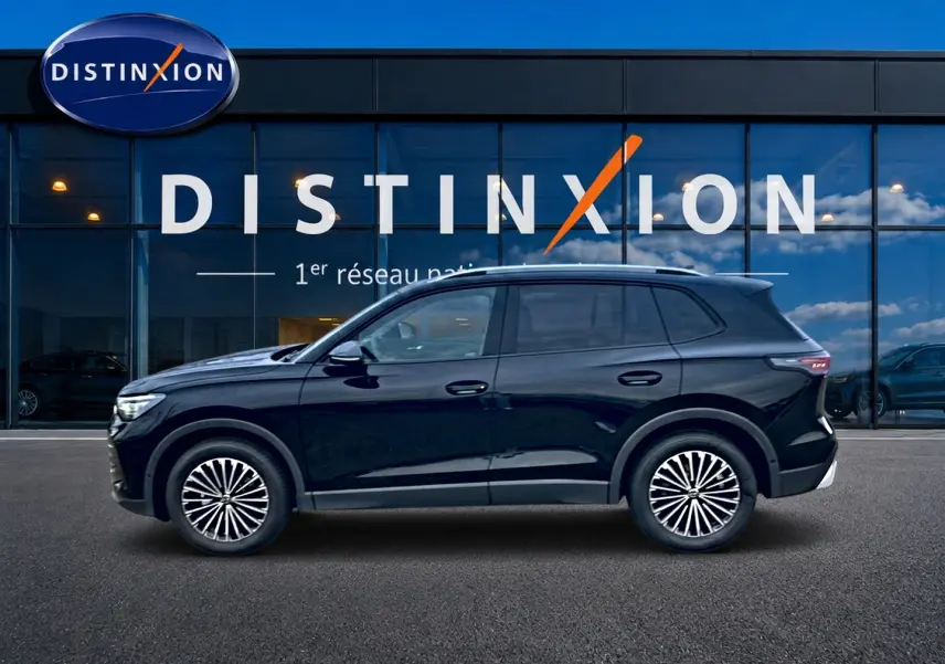 Vue de profil côté gauche d'un Volkswagen Tiguan noir 2025 garé devant une vitrine Distinxion.