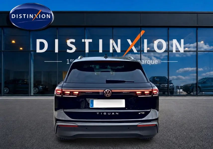 Vue arrière d'un Volkswagen Tiguan noir 2025 avec feux arrière LED et logo VW visible devant un bâtiment Distinxion.