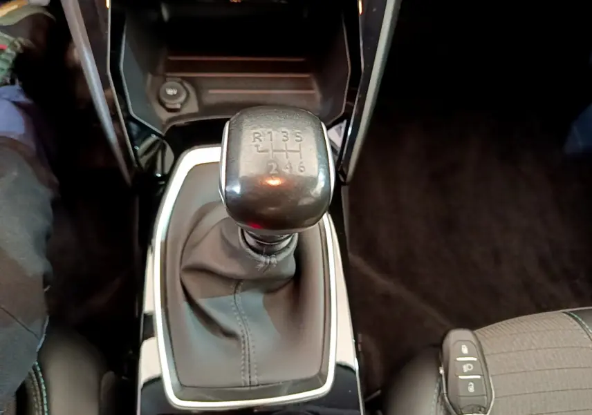 Gros plan sur le levier de vitesses manuel noir de la Peugeot 208 blanche, intérieur sombre avec siège tissu visible.