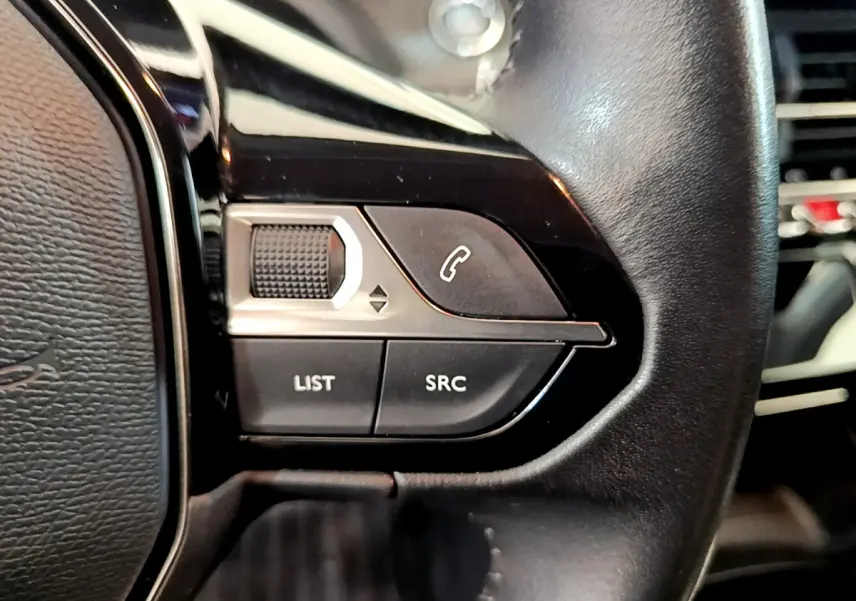 Gros plan sur les commandes gauche du volant cuir noir d'une Peugeot 208 blanche, boutons liste et appel visibles.