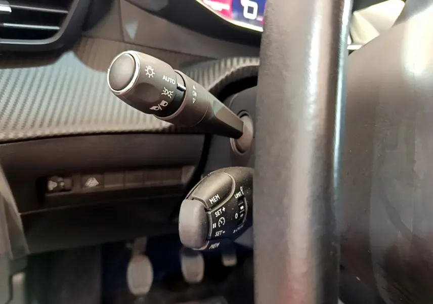 Gros plan sur les commandes au volant cuir de la Peugeot 208 blanc, avec leviers de clignotants et régulateur de vitesse.