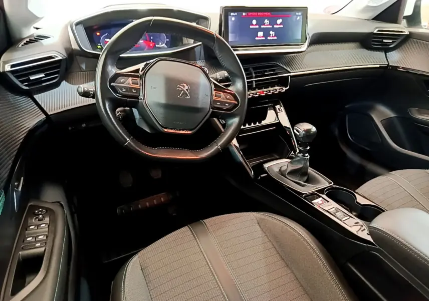 Vue intérieure avant de la Peugeot 208 PureTech 100 avec volant cuir, écran tactile et levier de vitesse manuel.