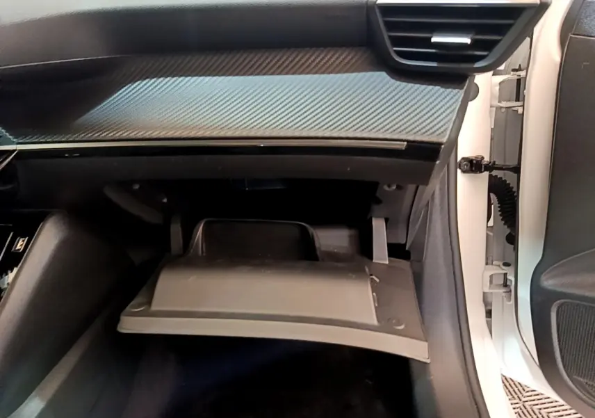 Vue intérieure côté passager du Peugeot 208 blanc 2020, boîte à gants ouverte sous tableau de bord noir avec insert carbone.