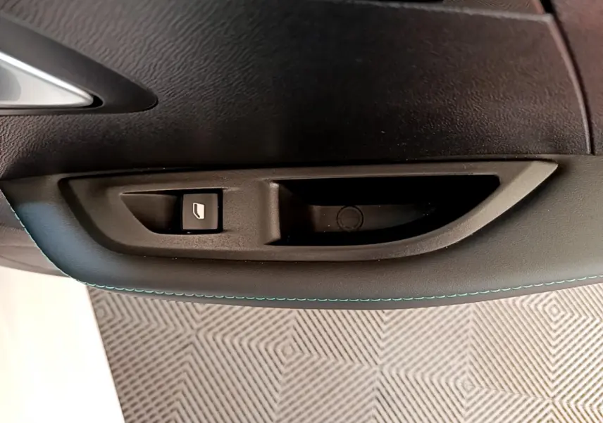 Gros plan sur la poignée intérieure et bouton de lève-vitre côté gauche d'une Peugeot 208 blanche, finition Allure Business.