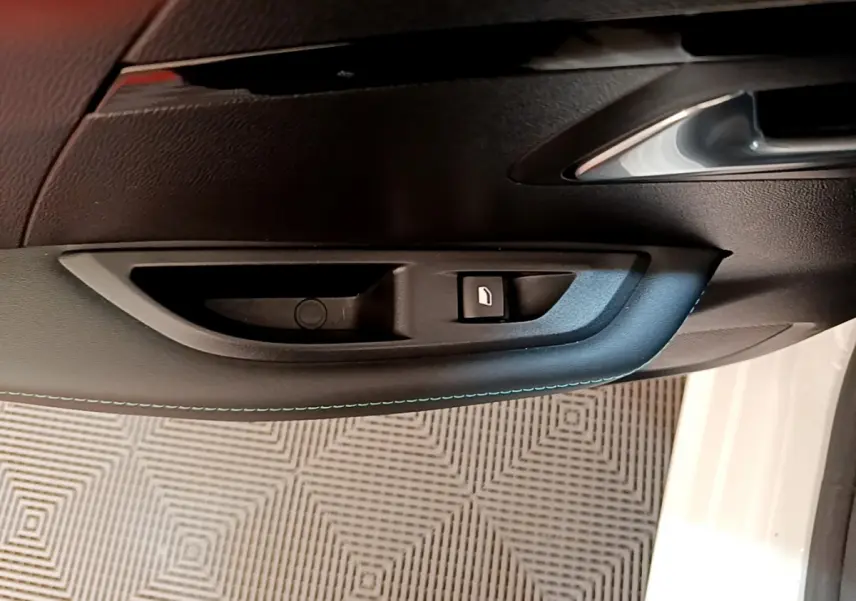 Gros plan sur la poignée intérieure côté gauche de la porte noire de la Peugeot 208 blanche, bouton de verrouillage visible.