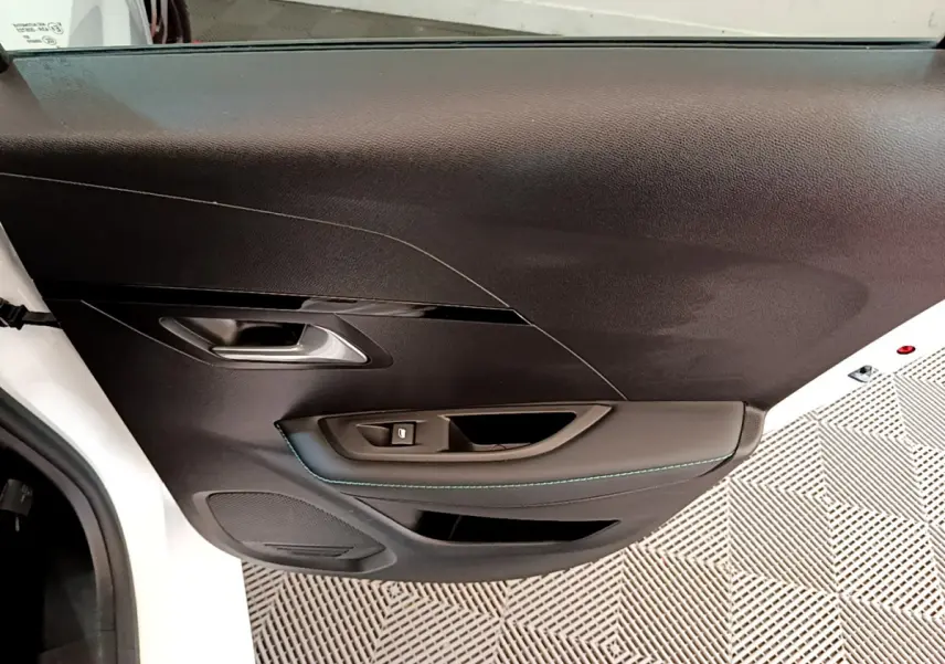 Vue rapprochée de la porte intérieure côté gauche noire avec surpiqûres bleues d'une Peugeot 208 blanche 2020.