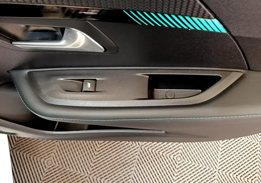 Gros plan sur la poignée intérieure côté conducteur de la Peugeot 208 blanche avec surpiqûres bleues et insert carbone.