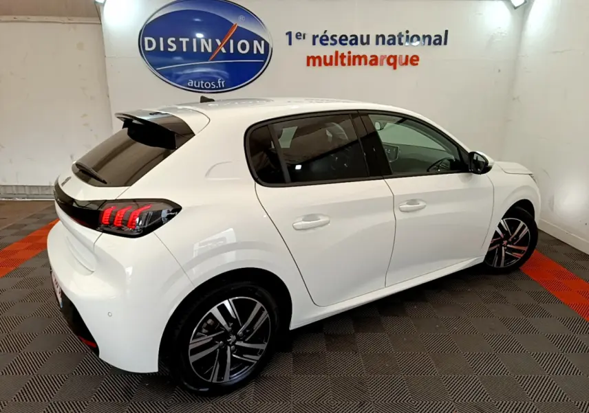 Peugeot 208 blanc vue 3/4 arrière droit en intérieur, feux arrière LED et jantes alliage distinctives visibles.