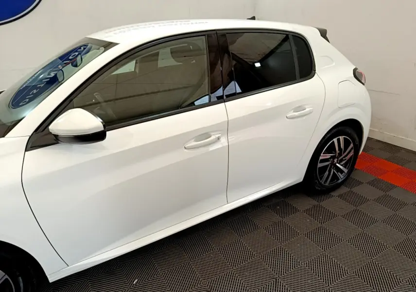 Profil côté gauche de la Peugeot 208 blanche de 2020, avec jantes alliage et vitres teintées dans un showroom.