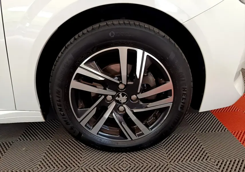 Gros plan sur la roue avant gauche blanche d'une Peugeot 208 2020 avec jante alliage bicolore et logo lion central.