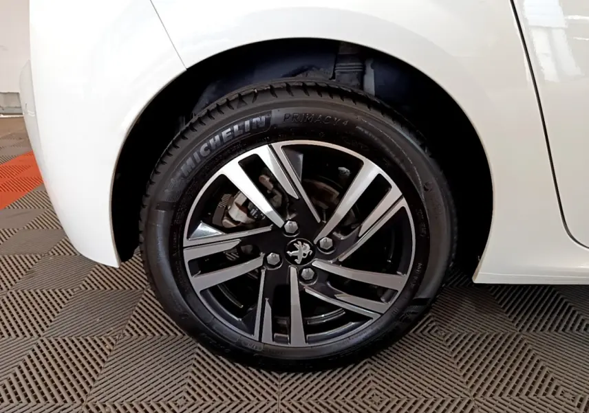 Gros plan sur la roue avant droite d'une Peugeot 208 blanche avec jante alliage noire et argentée.