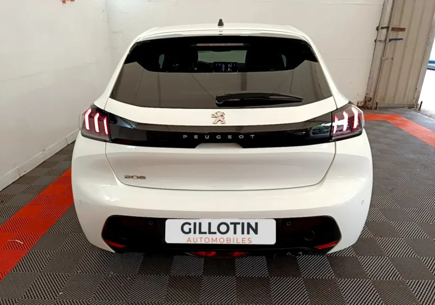 Vue arrière d'une Peugeot 208 blanche avec feux arrière LED distinctifs et logo Peugeot central sur bande noire.