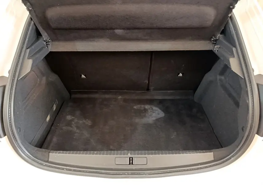 Coffre ouvert vu de l'arrière d'une Peugeot 208 blanche, montrant l'espace de chargement vide et la garniture noire intérieure.