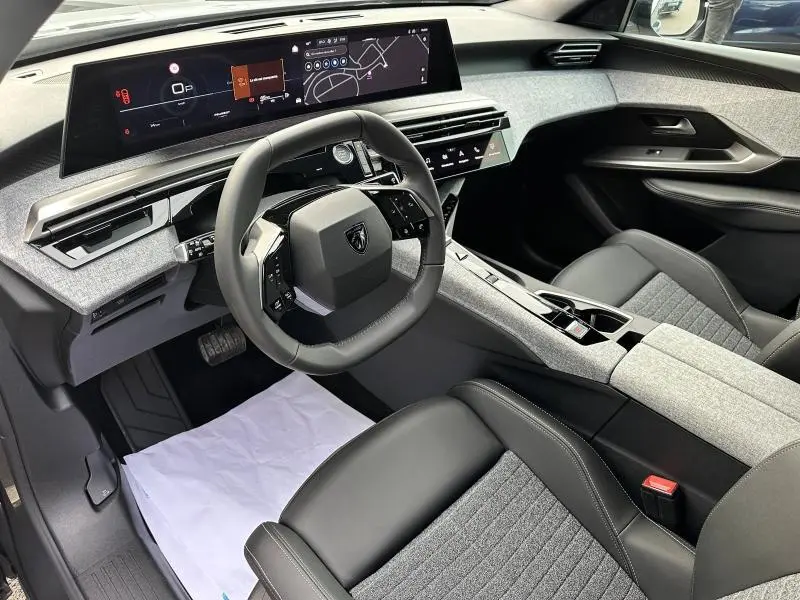 Vue intérieure côté conducteur du Peugeot 3008 Hybrid 2025 avec tableau de bord numérique et sellerie tissu gris et cuir noir.