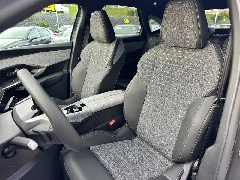 Vue intérieure côté conducteur du Peugeot 3008 Hybrid 2025 avec sièges tissu gris et cuir noir, accoudoir central visible.