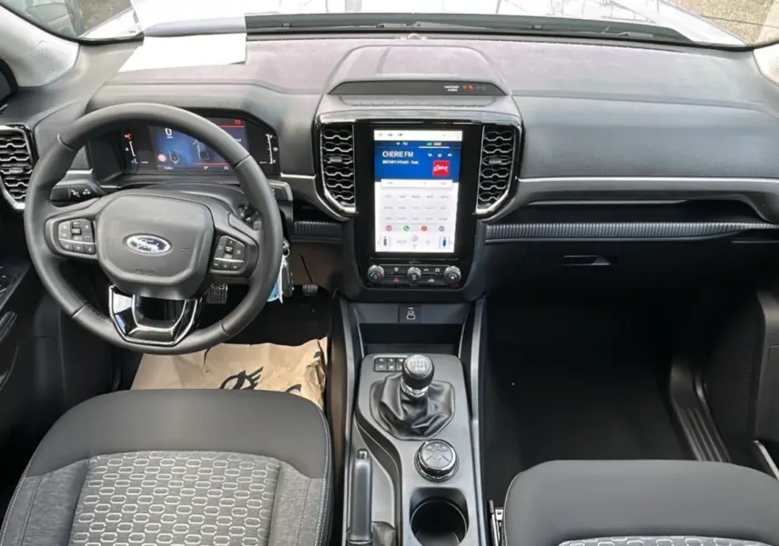 Vue intérieure frontale du Ford Ranger 2026 avec tableau de bord noir, écran tactile vertical et boîte manuelle.