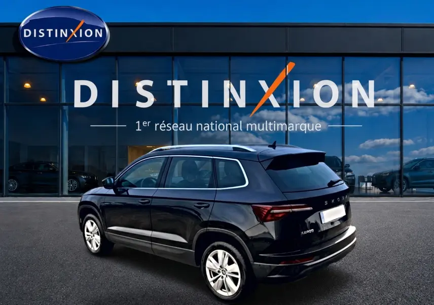 Vue 3/4 arrière droite d'un Skoda Karoq noir 2025 avec jantes alu, barres de toit et feux arrière LED, devant un showroom Distinxion.