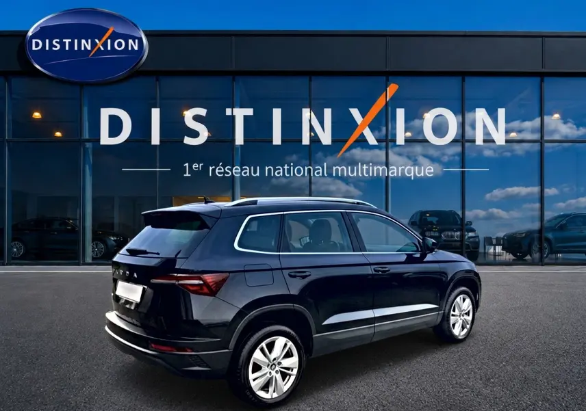 Vue 3/4 arrière droite d'un Skoda Karoq noir 2025 avec jantes alu, barres de toit et becquet arrière visible.