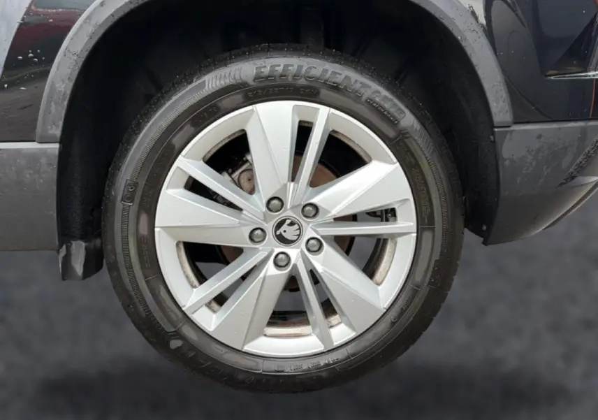 Gros plan sur la roue avant droite d’un Skoda Karoq noir avec jante alu argentée et logo Skoda au centre.