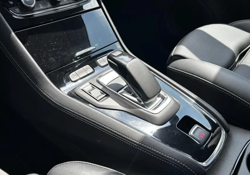 Gros plan sur la console centrale noire brillante de l’Opel Grandland 1.6 Hybrid avec levier de vitesse automatique et sièges cuir noirs.