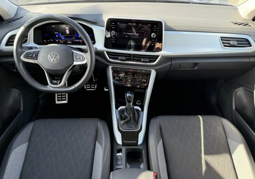 Vue intérieure frontale du tableau de bord et volant du Volkswagen T-Roc 2025 avec écran tactile et sellerie noire.