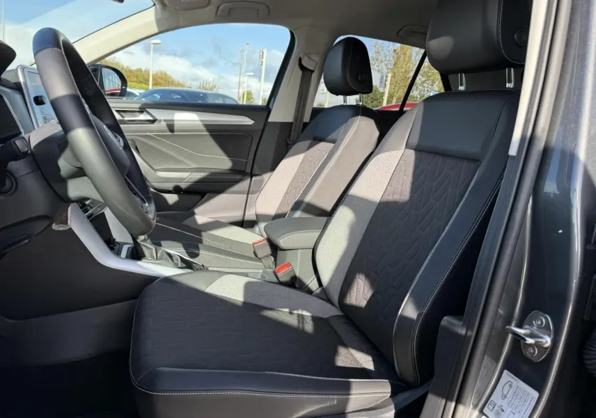 Vue intérieure côté conducteur du Volkswagen T-Roc 2025 gris Indium, sièges tissu et cuir noir avec coutures blanches.