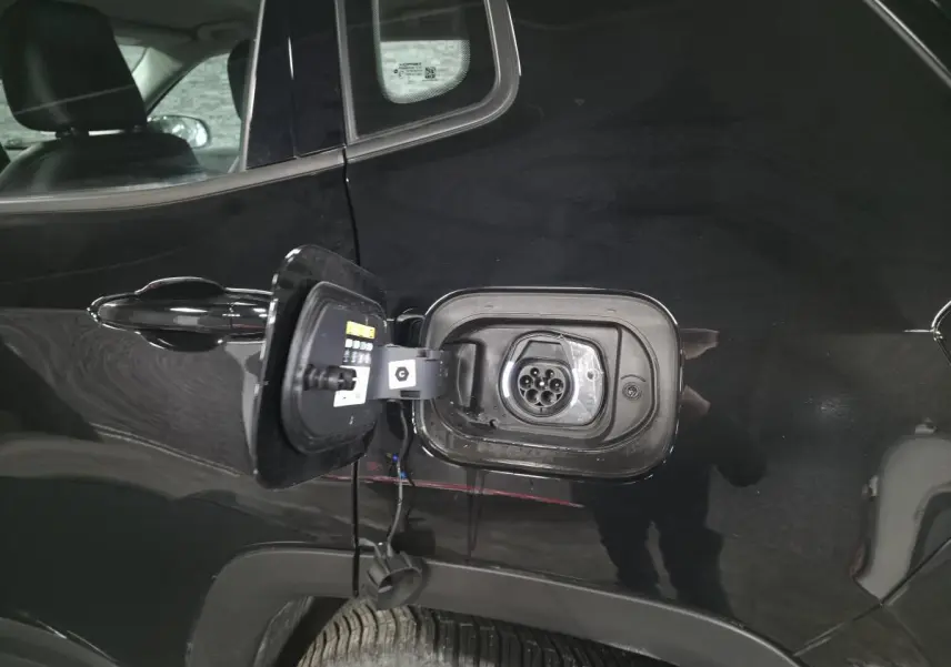 Prise de recharge ouverte côté arrière gauche d'un Jeep Compass noir hybride rechargeable 2024, détail de la trappe et connecteur.