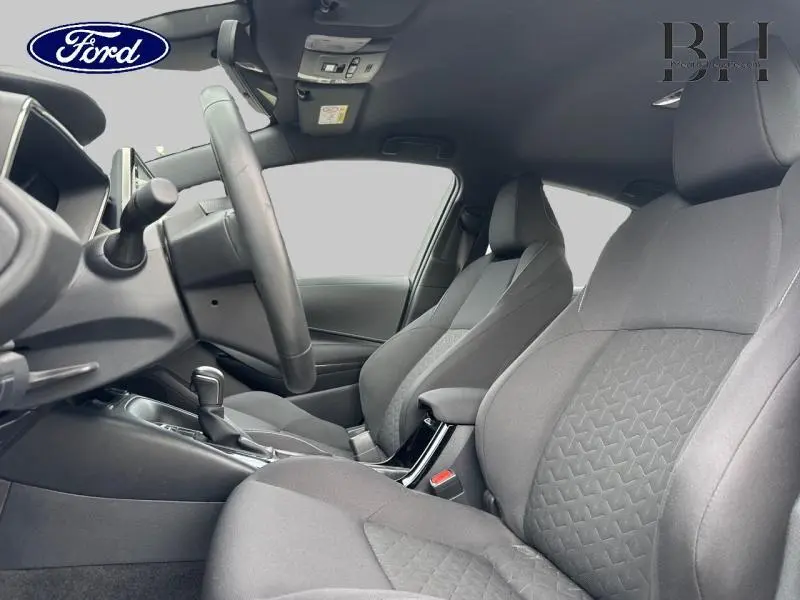 Vue intérieure côté conducteur montrant les sièges en tissu noir et le volant cuir de la Toyota Corolla gris Manhattan.