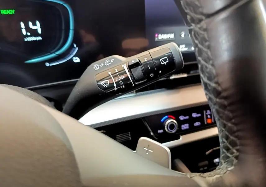 Gros plan sur le commodo d’essuie-glace et le volant cuir du tableau de bord du Kia Sportage blanc hybride rechargeable 2022.