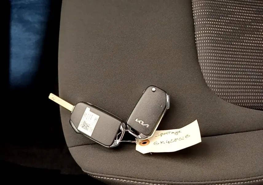 Clé de voiture KIA posée sur un siège tissu noir à l'intérieur d'un KIA SPORTAGE blanc, vue rapprochée.