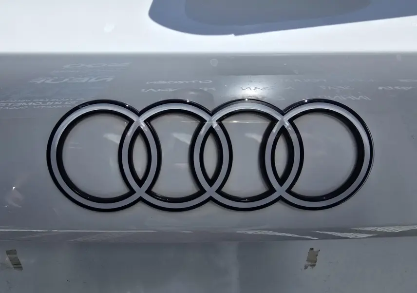 Gros plan sur le logo Audi noir brillant sur la carrosserie blanche Arkona d'une Audi A3 Sportback 2024.