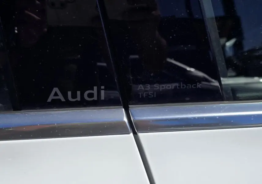 Gros plan sur les vitres arrière gauche d'une Audi A3 Sportback blanche avec logos Audi et TFSI visibles.