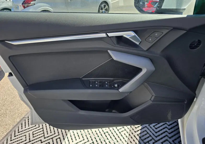 Vue intérieure du panneau de porte côté conducteur de l'Audi A3 blanc Arkona avec commandes électriques et poignée argentée.