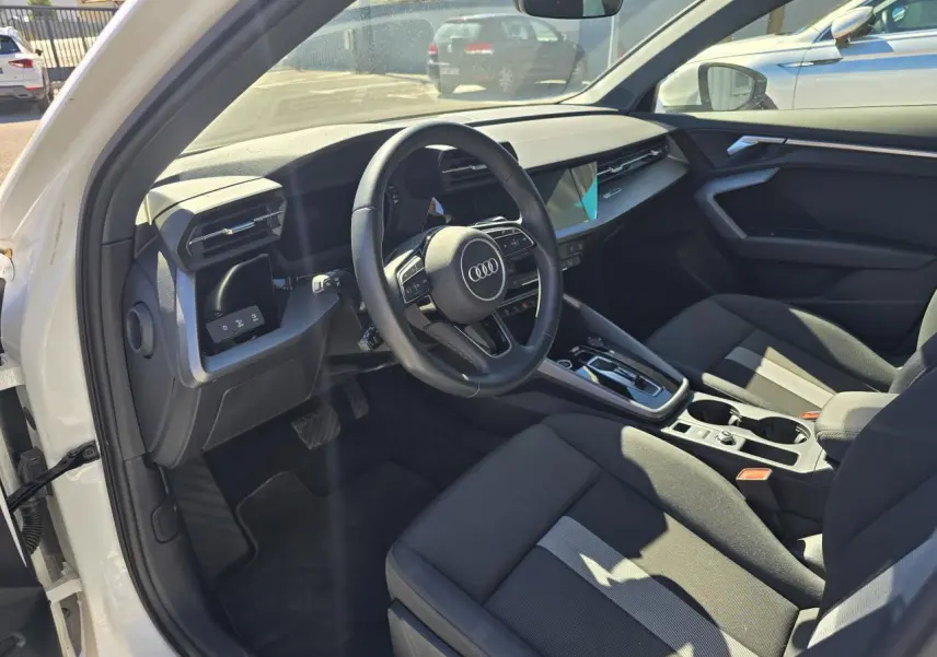 Vue intérieure côté conducteur de l'Audi A3 Sportback 2024 avec sièges noirs et volant multifonctions en cuir.