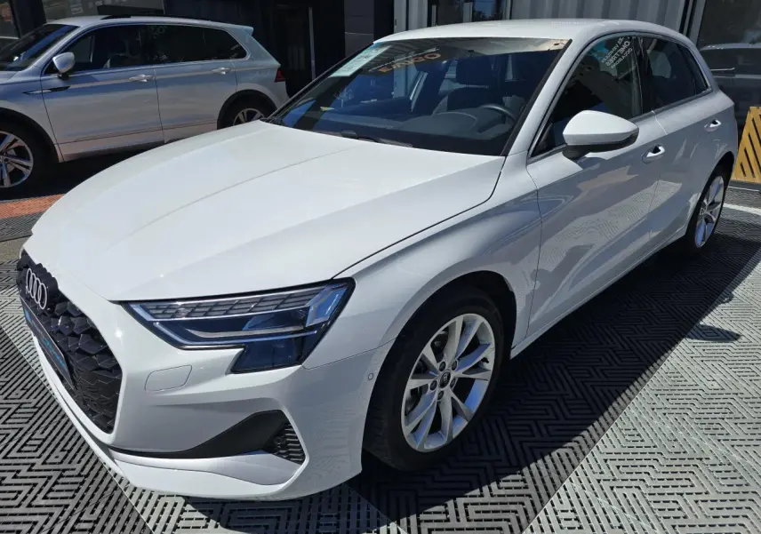 Audi A3 Sportback blanc Arkona vue 3/4 avant droit, avec jantes alliage 5 branches et phares LED distinctifs.