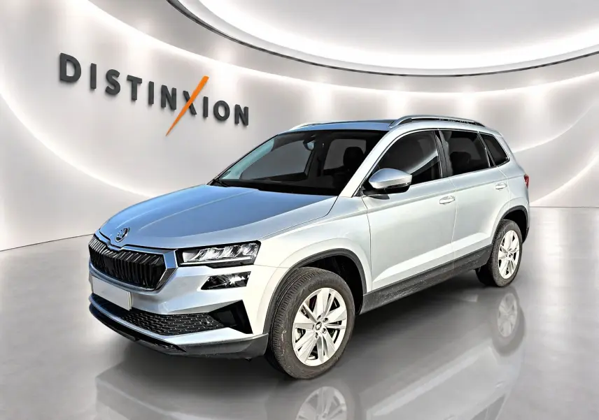 Vue 3/4 avant droite d'un Skoda Karoq gris 2025 avec calandre noire et jantes alu cinq branches.