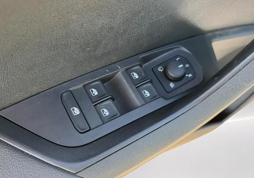 Gros plan sur les commandes des vitres et rétroviseurs côté conducteur d’un Skoda Karoq gris 2025.