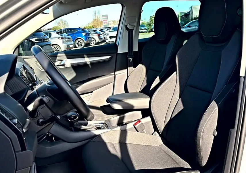 Vue intérieure côté conducteur du Skoda Karoq gris 2025, montrant sièges avant noirs et accoudoir central.