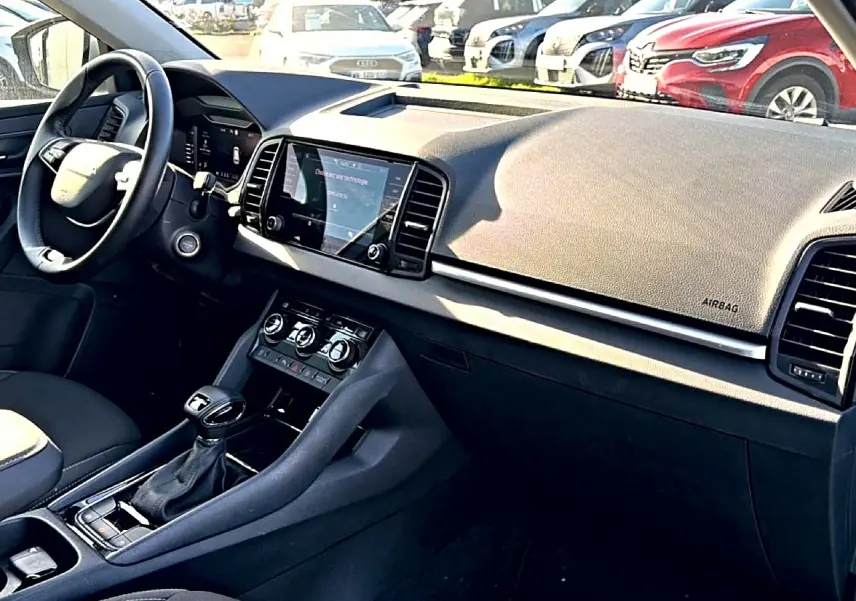 Vue intérieure côté conducteur du tableau de bord noir du Skoda Karoq 1.5 TSI 2025 avec écran tactile central et volant cuir.