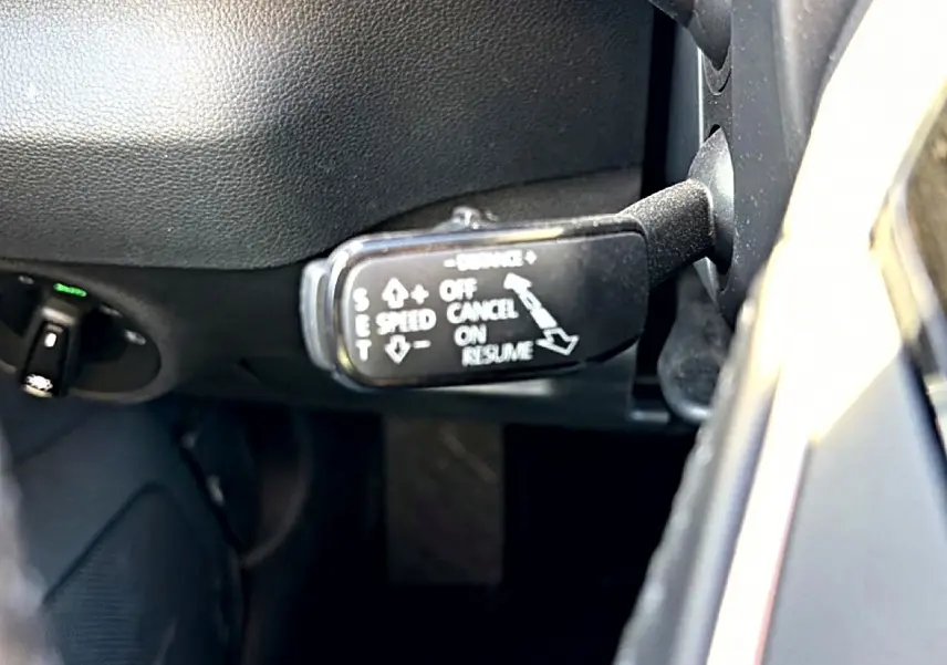 Gros plan sur la commande de régulateur de vitesse à gauche du volant dans l’habitacle gris du Skoda Karoq 2025.