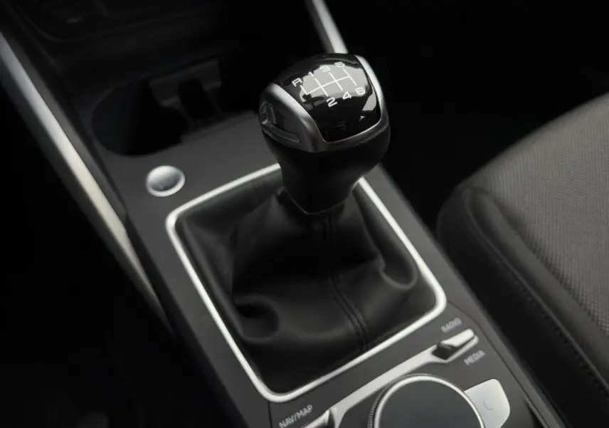 Gros plan sur le levier de vitesses manuel noir de l’Audi Q2 30 TFSI S-Line 2024, entouré de commandes grises.