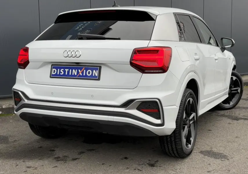 Audi Q2 30 TFSI S-Line blanc Glacier vue 3/4 arrière droit avec jantes noires et feux arrière LED distinctifs.