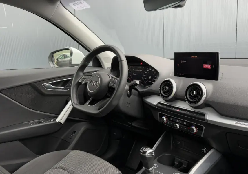 Vue intérieure côté conducteur de l'Audi Q2 30 TFSI S-Line 2024 avec volant cuir, écran central et boîte manuelle.